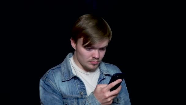 Elegante, jovem, moderno homem datilografando mensagem no celular, isolado no fundo preto. Jovem olhando para seu telefone inteligente enquanto mensagens de texto — Vídeo de Stock