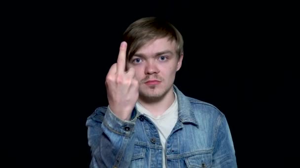 Homem de casaco de ganga azul está mostrando foda-se sinal com o dedo médio, isolado em fundo preto. Bonito, jovem mostrando dedo médio gesto parafuso você . — Vídeo de Stock
