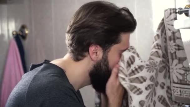 Мужчина вытирает лицо полотенцем. День начинается с заботы о лице. Крупный план красивого бородатого мужчины, моющегося в ванной утром — стоковое видео