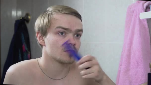 Молодий чоловік розчісує волосся вранці у ванній. Ранкова рутина. Чоловік з щетиною розчісує волосся і дивиться у дзеркало — стокове відео
