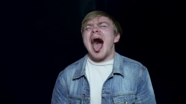 Junger Mann, der mit herausgestreckter Zunge schreit. junger Mann mit hervorstehender Zunge. menschliche Mimik und Emotionen. schwarzer isolierter Hintergrund — Stockvideo