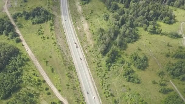 Platteland weg omgeven door weelderige groene natuur. Clip. Bovenaanzicht van landelijke weg in bos. Verkeer op landelijke wegen — Stockvideo