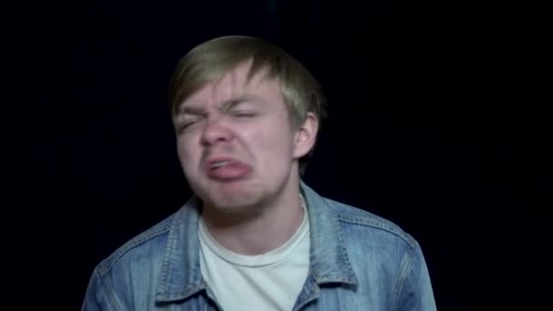 Man showing his tongue. Young man angrily grimaces and out tongue. Human facial expressions and emotions. Black isolated background — Stock Video