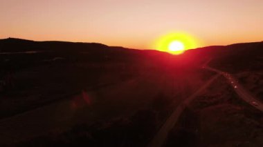 Kırmızı günbatımı. Vurdu. Kırmızı günbatımı gökyüzü ile kısmen dağlarla gizli güneşin parlak yuvarlak yüzey. Sunset Bulvarında kırsal alanın içinden geçen kırsal karayolu üzerinde trafik üstten görünüm