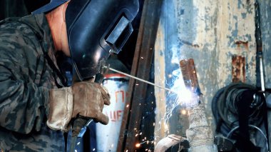 Kaynakçı Kaynak maskesi fabrikasında metal parçalar kaynak. Çerçeve. Maskeli Kaynakçı Kaynak parçaları. Mavi ve sarı ile kaynak kıvılcımlar