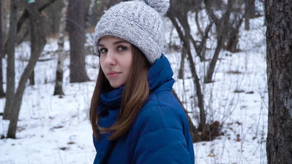 Молодая женщина ходит зимой. Привлекательная женщина в зимней шляпе гуляет в парке среди деревьев и снега. Красивая женщина, печально вдумчивая, глядя на его ноги, идущие в одиночку — стоковое фото