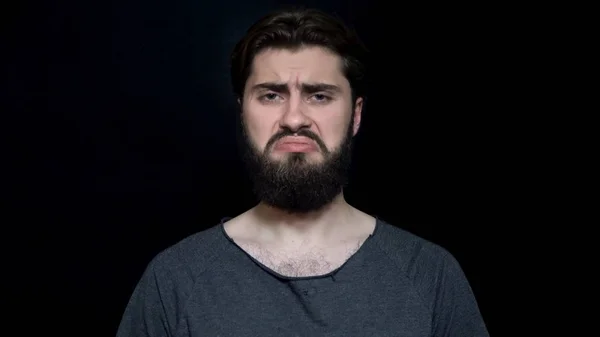 Mies, jolla on parta, paheksuu surullisesti ja järkyttyneenä. Nuori parrakas mies näyttää surulliselta ja loukkaantuneelta. Ihmisen ilmeet ja tunteet — kuvapankkivalokuva