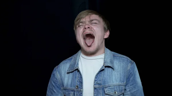 Un joven gritando con la lengua extendida. Joven con lengua sobresaliente. Expresiones faciales y emociones humanas. Fondo negro aislado — Foto de Stock