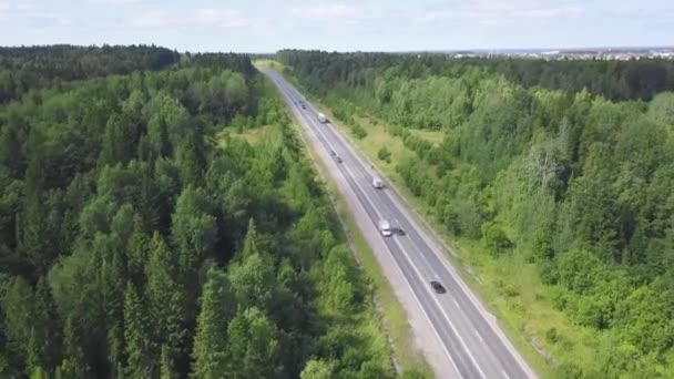 Bovenaanzicht van de weg in het bos. Clip. Verkeer op landelijke weg met stad op achtergrond in bewolkte hemel — Stockvideo