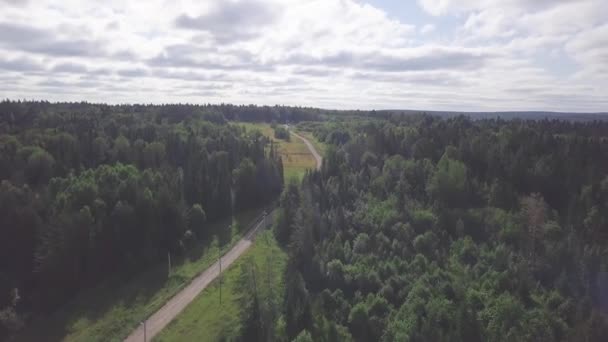 Вид сверху сельской дороги в лесу и облачном небе. Клип. Небольшой домик в лесу рядом с сельской дорогой. Уединенная жизнь в лесу за городом — стоковое видео