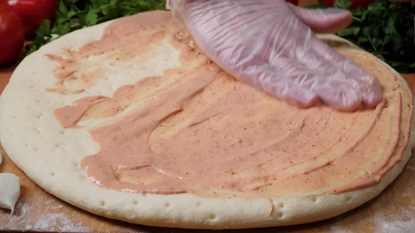 Lägga till sås. Italiensk pizza beredning. Ram. Ost som sprids på tomatsåsen på pizzabotten. Närbild hand kock Baker i vit uniform att göra pizza på kök — Stockfoto