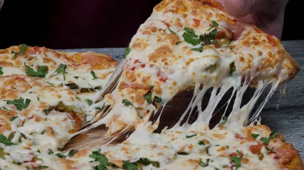 Время обеда в пиццерии, человек берет кусочек пиццы с очень тонкой глубиной резкости. Рамка. Рука режет кусок пиццы и принимает его, крупным планом, макро выстрел. Пицца и ломтик пиццы в руке на — стоковое фото