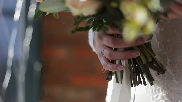Όμορφη νυφική ανθοδέσμη στα χέρια του νεαρή νύφη ντυμένη με λευκό νυφικό. Νύφη χέρι αγγίζει τα γαμήλια ανθοδέσμη. Κοντινό πλάνο του μεγάλο μάτσο φρέσκα λευκά τριαντάφυλλα και τουλίπες λουλούδια στα γυναικεία χέρια — Φωτογραφία Αρχείου
