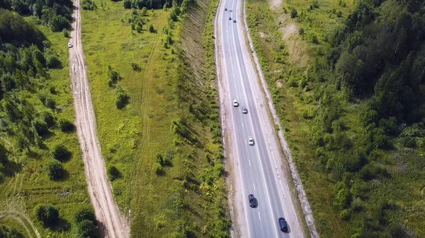 Aerial top view of summer green trees, river, roads in forest background. Aerial view of crooked path of road on the mountain. Clip. Aerial view of cars driving on country road in forest. The aerial