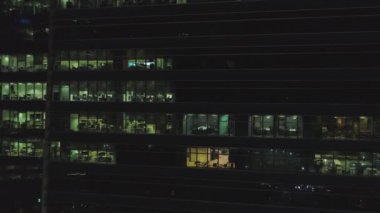 Gece cephe ışıklı windows bir sürü binanın ön görünümü. Vurdu. Dış cephe cam ve çelik, ofisler ve çalışan insanlar içinde gece şehir hayatı arka plan çok katlı bina