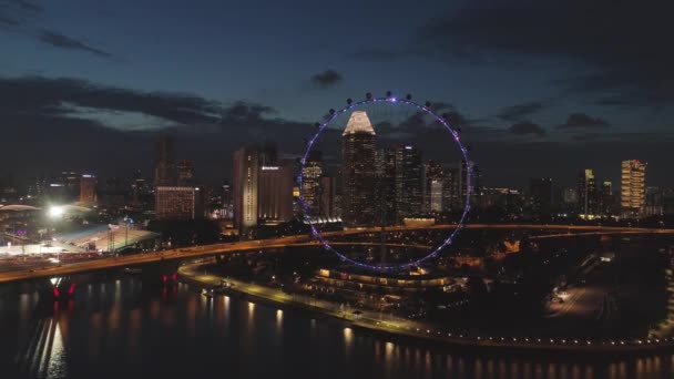 Singapore - 25 September 2018: Flygfoto över storstad med många lampor, molnig himmel och pariserhjul på natten. Skott. Vackra stora staden bakom sjön vid natt med utsikt över ett pariserhjul och många — Stockvideo