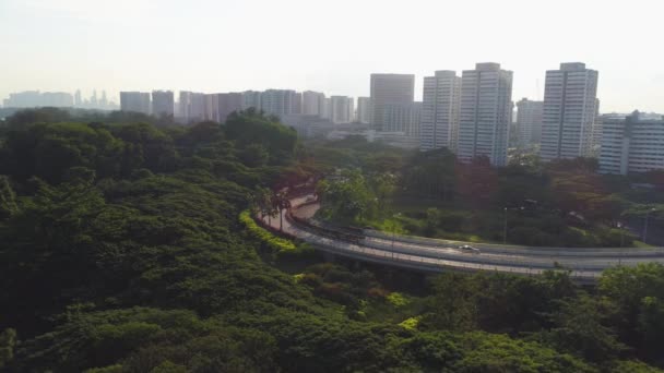 Aéreo para rotunda com floresta verde em um lado da estrada e edifícios de vários andares no outro. Atingido. Vista aérea da estrada redonda na cidade no verão . — Vídeo de Stock