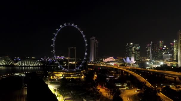 Singapur - 25 de septiembre de 2018: Ciudad de Singapur skyline por la noche con el río, noria iluminada púrpura y famoso Marina Bay Sands Hotel. Le dispararon. Impresionante vista aérea de la noche Singapur con — Vídeos de Stock