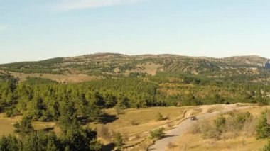 Havadan görüntüleri güneş yeşil alanlar arasında bir yolda sürme bir araba ayarlayın. Vurdu. Yeşil tepelerin ve araba sürüş hızlı olan yol üzerinde casus uçak uçar. Köy yolunda hava üstten görünüm.