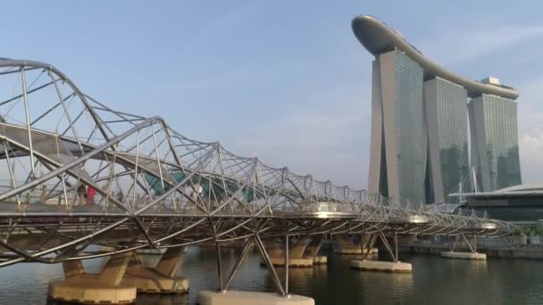 曇りの日のマリーナ ベイ サンズ ホテルにステンレスの橋で覆われているシンガポールでシンガポール - 2018 年 6 月 28 日: コンクリート。昼間のシンガポール都市。ヘリックス ・ ブリッジとマリーナ湾の砂 — ストック動画