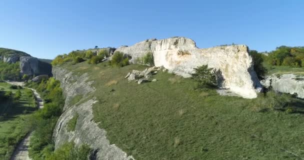 Камень над ущельем. Выстрел. Вид сверху на ландшафт каменного хребта, голубое небо и зеленое ущелье. Солнечный день в горном ущелье — стоковое видео