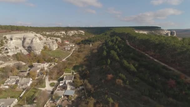 Luftaufnahme von felsigen Klippen, Wald und kleinem Dorf vor blauem Himmel. Schuss. Frühherbstlandschaft — Stockvideo