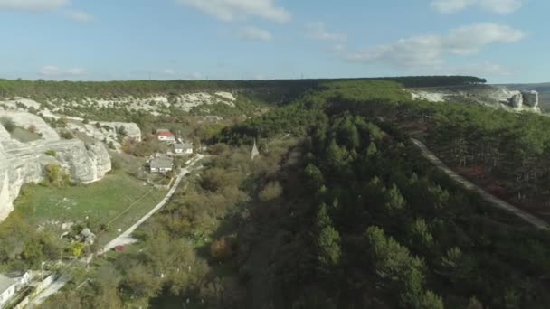 Luchtfoto van rotswanden, bos en dorp tegen blauwe hemel. Schot. Vroege herfst landschap — Stockvideo