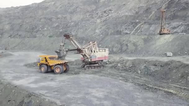 Excavadora y camión volquete mientras carga mineral de piedra en una cantera gris, industria minera. Acciones. La excavadora pesada carga mineral de roca en un camión minero grande de cuerpo volcado, equipo de cantera . — Vídeos de Stock