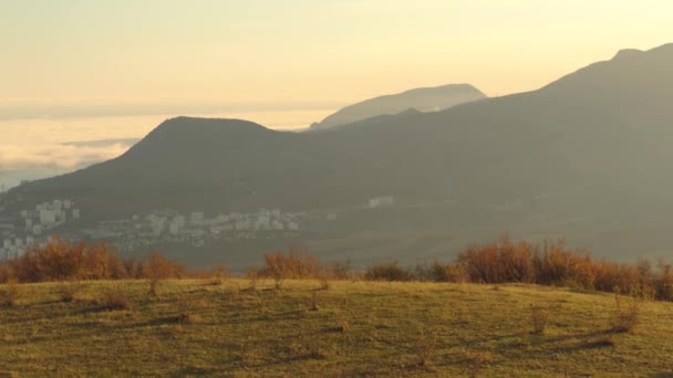 Vista panoramica della pittoresca valle autunnale da un ripido pendio cespuglioso sullo sfondo del cielo al tramonto. Gli hanno sparato. Spettacolare vista sulle montagne di un piccolo villadge e un campo al tramonto luce dorata . — Video Stock