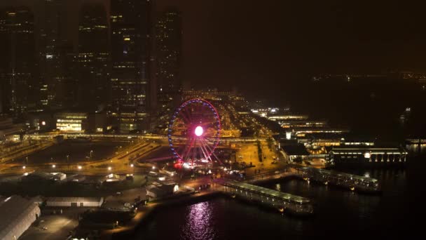 Una vista nocturna del muelle, el río, la noria y la hermosa ciudad nocturna. Acciones. Rueda ferris iluminada púrpura cerca del río sobre fondo nocturno de la ciudad . — Vídeo de stock