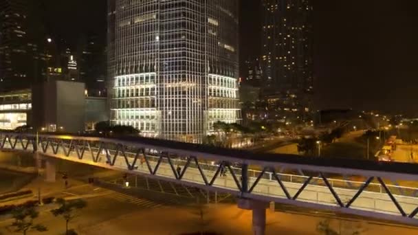 Pasarela con transeúntes por encima de la carretera en el fondo de la ciudad de noche. Acciones. Puente peatonal con gente caminando por los edificios nocturnos de la ciudad . — Vídeo de stock