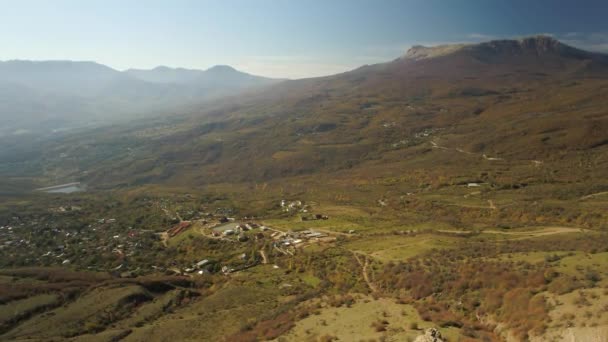 Luchtfoto alpenlandschap van een klein dorpje in de bergen met blauwe hemel en herfst geel gras. Schot. Kleurrijke herfst landschap van een dorpje in een vallei in de Alpen. — Stockvideo