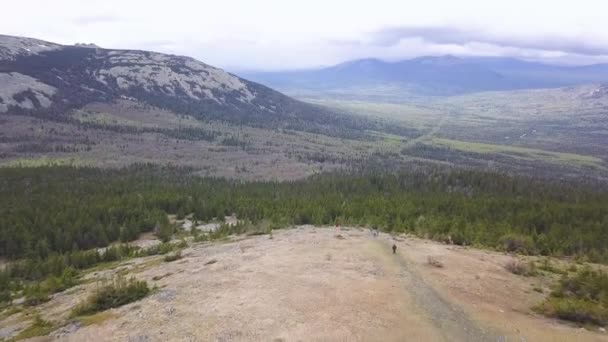 Vista superior del valle con paisaje de montaña en el horizonte. Clip. Sendero sendero con excursionistas en la zona forestal en el fondo de las montañas y el cielo nublado. Descanso activo en la naturaleza — Vídeo de stock