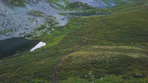 Légi felvétel a kék tó tükrözi a gyönyörű hegyekkel a háttérben. Klip. Légifelvételek lenézett hegyi tavak és patakok, zöld fű és miountains háttér — Stock Fotó