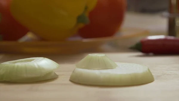 Caduta di cipolle ad anello tagliate a fette su tagliere di legno. Primo piano di cerchi cadenti di cipolla verde su ciotola di vetro da tagliere, al rallentatore. Porro affettato che cade sulla scrivania di legno per affettare il cibo — Foto Stock