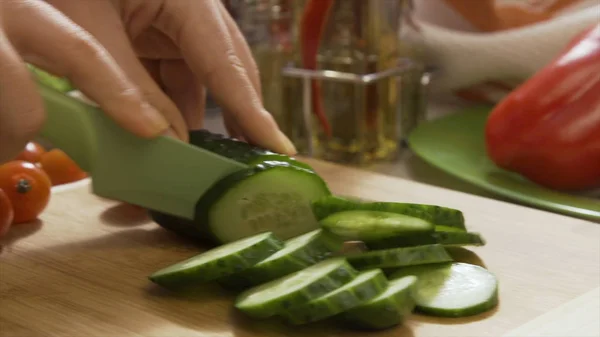 Primo piano di mano con coltello taglio cetrioli su tavola di legno. Scena. Cetriolo fresco su un tagliere di legno. Colpo ravvicinato di cetriolo intero, disposizione o pila. Preparazione dell'insalata - taglio — Foto Stock