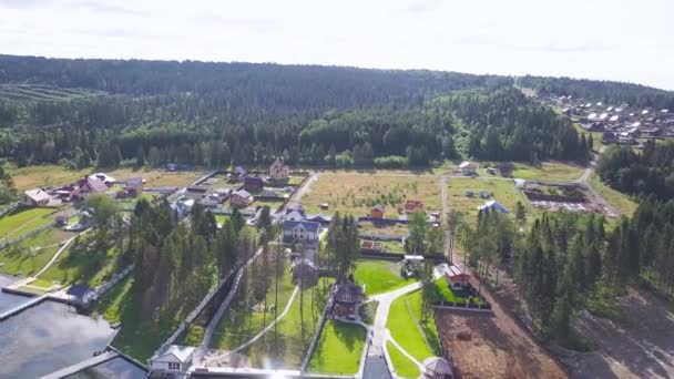 Vista superior de aldea de la cabaña por el lago. Clip. Casas rurales modernas con zonas de césped verde de pie en la orilla del lago en el fondo de bosque denso. El descanso en el campo en la temporada de verano — Vídeos de Stock