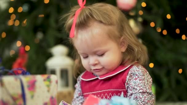 Jolie petite fille près du nouvel arbre de l'année. Petite fille sourit et joue avec des cadeaux sur le fond des arbres de Noël. Belle fille en robe près de l'arbre de Noël . — Video