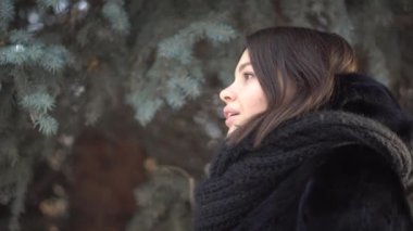 Çam ağaçları yakınındaki bir kış ormandaki siyah kürk paltolu güzel genç kız profil. Yakın çekim.