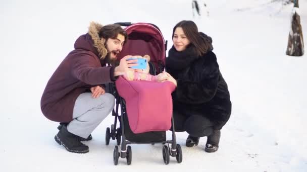 Coppia di famiglia seduta vicino alla carrozzina e fare selfie nella foresta invernale. Momenti felici . — Video Stock