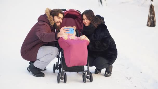 Para rodzina siedzi w pobliżu wózek dziecięcy i podejmowania selfie w zimowym lesie. Szczęśliwe chwile. — Wideo stockowe