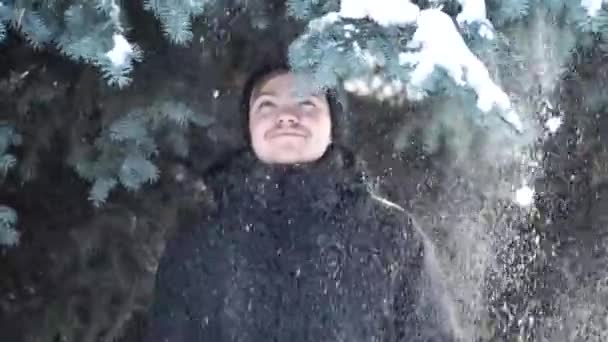 Close-up de um cara, ficando sob os ramos movendo-se abeto de neve. Ele está sorrindo. . — Vídeo de Stock