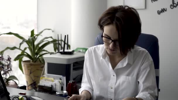 緑の植物とプリンターの近くビジネス論文に取り組んでいる白シャツの魅力的な若いオフィス女性 女性事務員のオフィスの机の上の書類を整理 — ストック動画