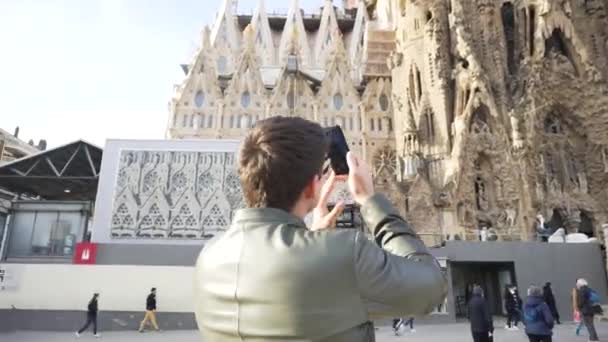 Espanha - Barcelona, 12 de agosto de 2018: Homem de jaqueta de couro e óculos escuros fotografando a fachada da catedral gótica em um dia ensolarado. Estoque. Jovem turista tira uma foto de estilo gótico — Vídeo de Stock
