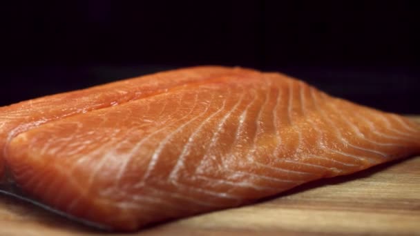 Un trozo de pescado fresco, crudo y rojo sobre una tabla de cortar marrón de madera, aislado sobre fondo negro. Hermoso filete de salmón acostado sobre tabla de cortar de madera, cocina y dieta saludable cocnept . — Vídeos de Stock