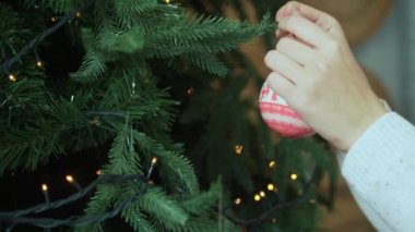 Kadın Noel top bokeh ışıklı ağaç üzerinde asılı. Bir kadının yakın çekim çekim eller, kim bir Noel dekorasyon, oyuncak Noel ağacı üzerinde asılı bir Bayan tutuyor. Noel dekorasyon el