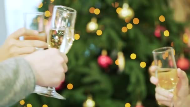 Company is holding glasses with champagne and clink, christmas tree on the background. Christmas, celebration and holidays concept - happy team clinking glasses of sparkling wine at party — Stock Video