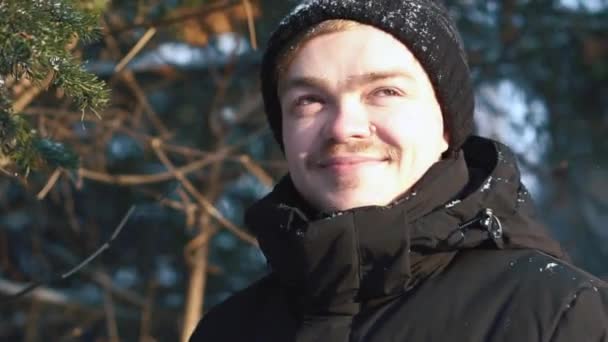 Jeune homme souriant dans une veste noire regardant loin dans la forêt d'hiver. Gros plan . — Video