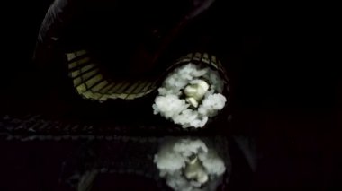 Suşi işlemini izole siyah arka plan üzerine siyah bambu makisu ile çalışırken. Ellerinde siyah eldiven ile siyah bambu hasır, kavram yemek suşi haddeleme.