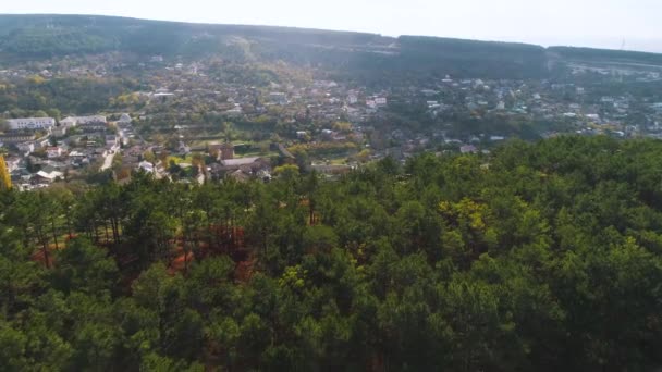 Vista superior de la ciudad en valle con colinas cerca del bosque. Le dispararon. Frontera de bosque verde y ciudad en estribaciones de colinas. Día soleado en la ciudad de montaña verde. Entorno urbano cerca de la naturaleza — Vídeos de Stock